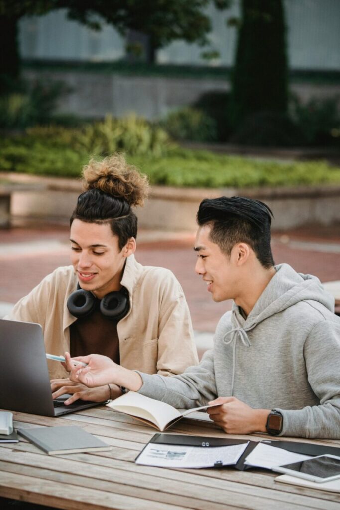 Two multicultural male students collaborate outside, engaged in a laptop-based project on campus.